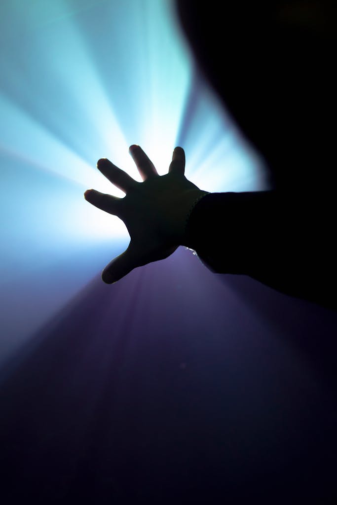 Silhouette of a hand reaching towards bright beams of light, creating a dramatic effect.